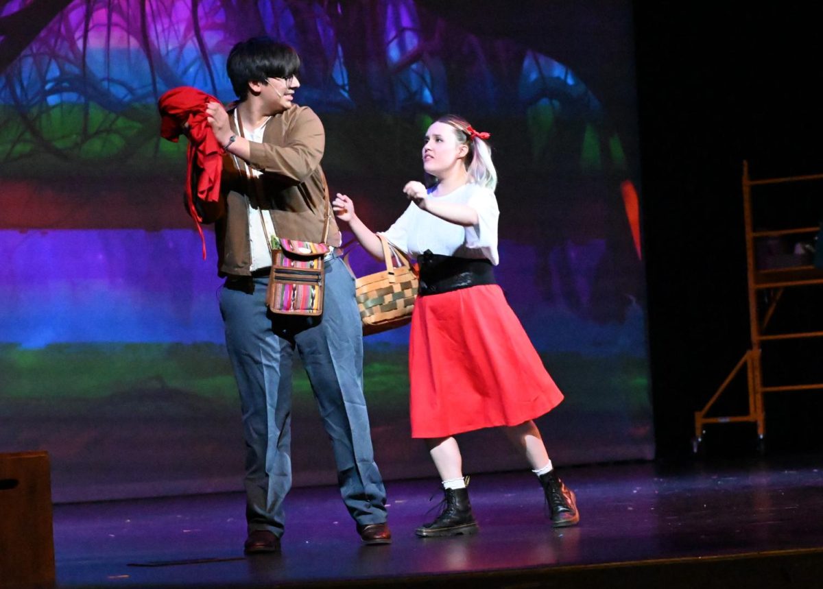 The photo shows Little Red Riding Hood getting her cape stolen by the Baker.